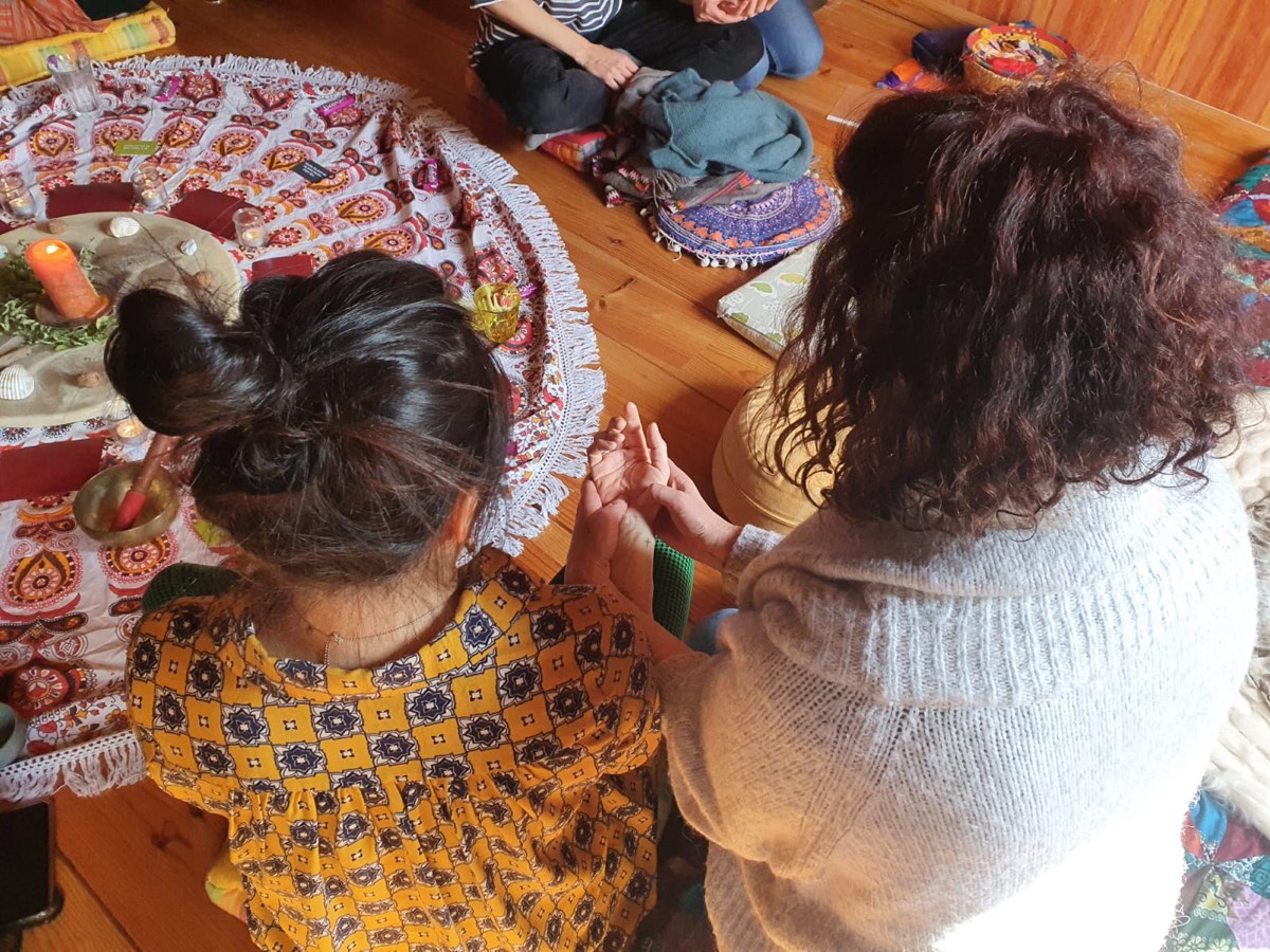 Des femmes assises au sol pendant un atelier, les mains jointes, autour d’un tissu orné de bougies